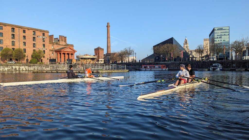 Two Men's doubles talking in their boats on the water. Pictured on the Liverpool Waterfront in Albert Dock.
